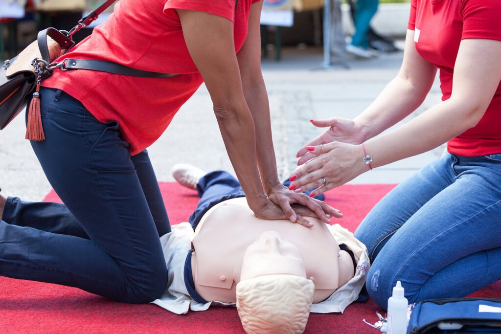 Instructor guiding community CPR practice on an adult training manikin